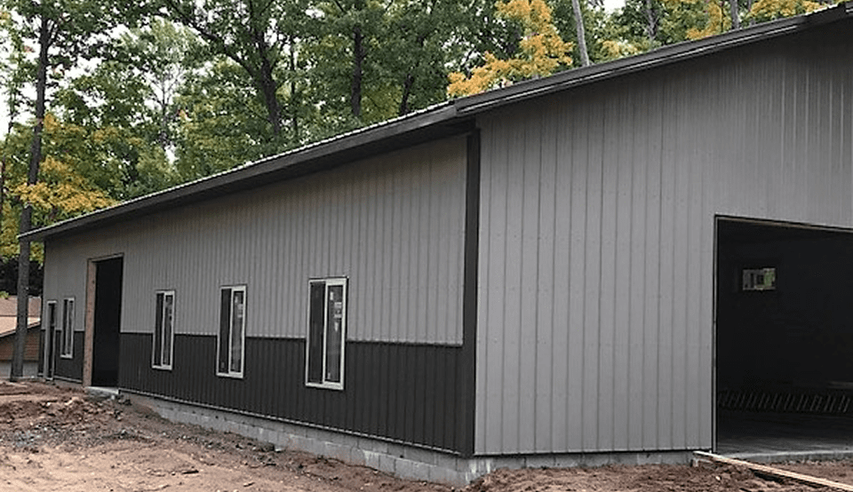 A gray building with vertical siding and small windows in a wooded area.